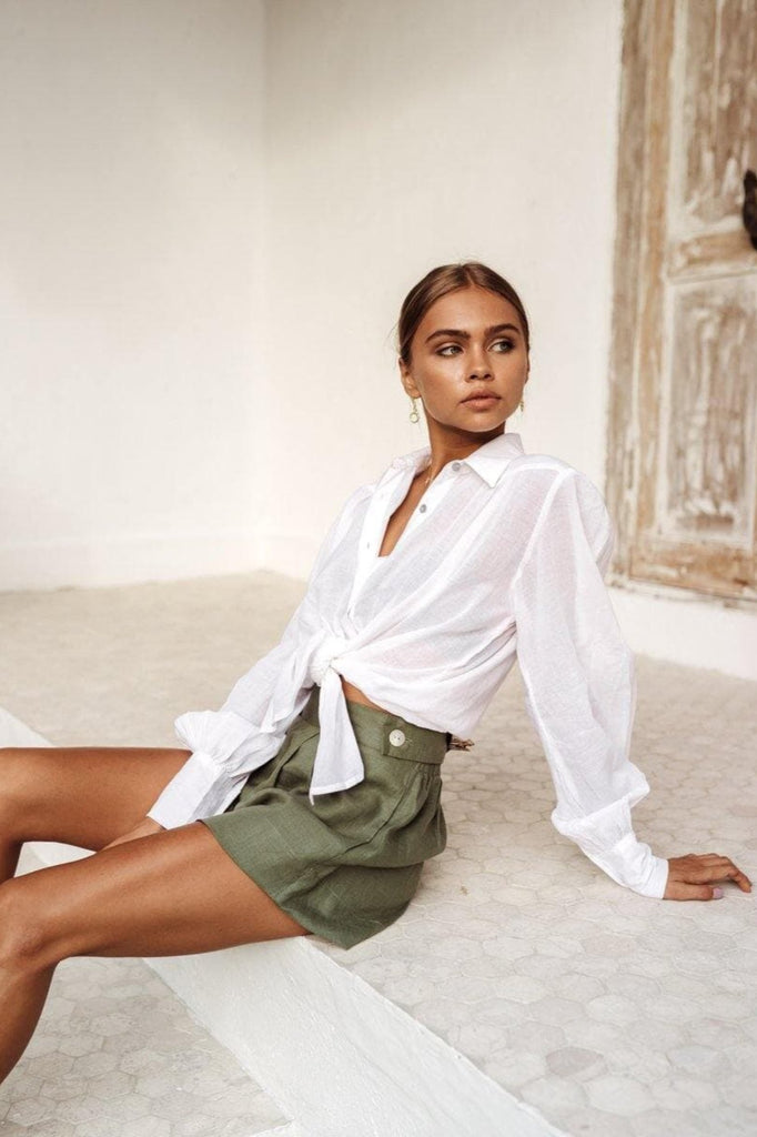 tan model sitting on a bench in linen shorts and a white classic shirt